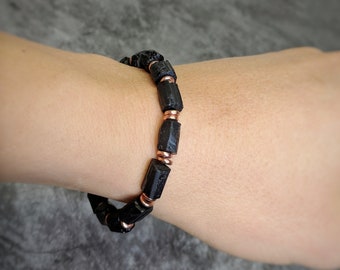 May include: Black Tourmaline bracelet with copper accents. The bracelet is made of black beads with a rough, natural texture. The copper accents are small and round, and they are spaced evenly along the bracelet.
