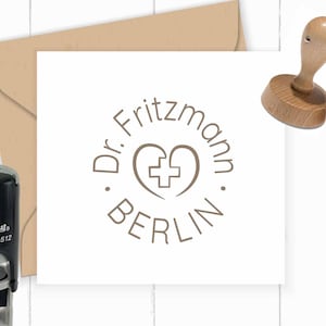 May include: A round rubber stamp with a brown ink pad. The stamp features a circle with the text "Dr. Fritzmann Berlin" and a heart with a plus sign inside. The stamp is on a white surface.