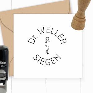 May include: A white card with a black and white circular stamp that says "Dr. Weller Siegen" with a medical symbol in the centre. The stamp is on a white card with a brown envelope behind it.