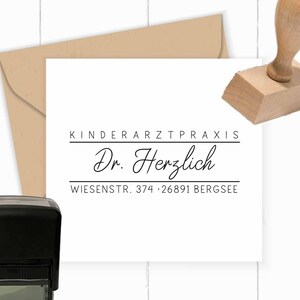 May include: A white card with black text and a kraft paper envelope. The text reads "KINDERARZTPRAXIS Dr. Herzlich WIESENSTR. 374 • 26891 BERGSEE". A wooden stamp and a self-inking stamp are also visible.