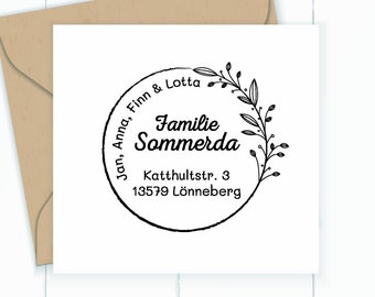 Pode incluir: Um carimbo quadrado branco com texto preto e um design floral, com as palavras "Familie Sommerda" e os nomes "Jan, Anna, Finn & Lotta". O carimbo inclui um endereço: "Katttultstr. 3, 13579 Lönneberg". Um envelope castanho está no fundo.