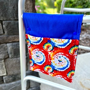 May include: A blue and red fabric pouch with tie-dye print hangs on a silver walker. The pouch has a blue flap with snaps.