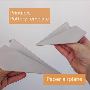 Pode incluir: Dois objetos cinza-claros, planos e rígidos em forma de aviões de papel. O texto "Printable Pottery template" e "Paper airplane" é exibido em branco sobre fundos retangulares laranja sobrepostos à imagem.