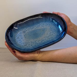 Può includere: Un piatto da portata ovale in ceramica caratterizzato da un bordo blu navy profondo che sfuma in un centro blu più chiaro e screziato con un distinto motivo a smalto crepato simile a una ragnatela. La ciotola ha una finitura lucida.