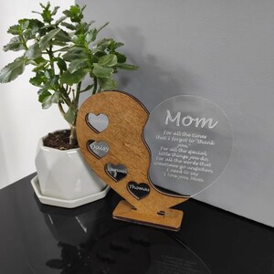 May include: A wooden heart-shaped plaque with a clear acrylic circle attached. The acrylic circle has the text "Mom, For all the times that I forgot to "thank" you, For all the special little things you do, for all the words that sometimes go unspoken, I need to say "I love you, Mom" engraved on it. The wooden heart has four smaller hearts with the names "Ember", "Daisy", "Samuel", and "Thomas" engraved on them.