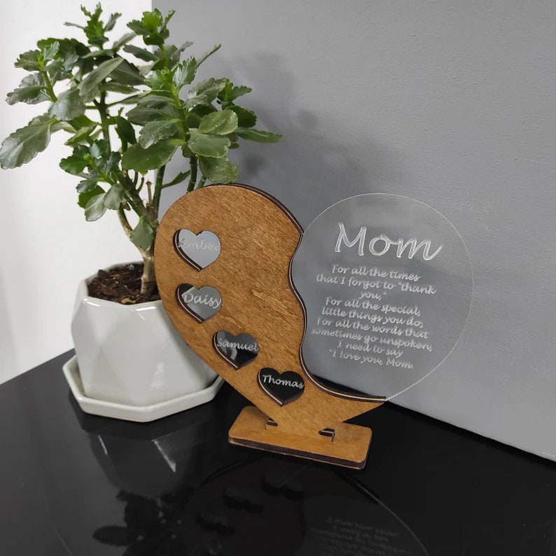 May include: A wooden heart-shaped plaque with a clear acrylic circle attached. The acrylic circle has the text "Mom, For all the times that I forgot to "thank" you, For all the special little things you do, for all the words that sometimes go unspoken, I need to say "I love you, Mom" engraved on it. The wooden heart has four smaller hearts with the names "Ember", "Daisy", "Samuel", and "Thomas" engraved on them.
