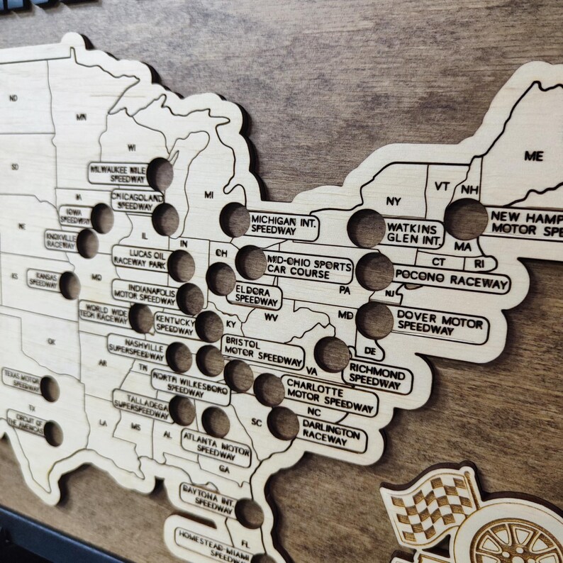 Pu&ograve; includere: Una mappa in legno degli Stati Uniti con dei buchi che rappresentano diversi circuiti NASCAR. La mappa &egrave; etichettata con i nomi di ogni circuito, tra cui il Daytona International Speedway, il Talladega Superspeedway e il Charlotte Motor Speedway.
