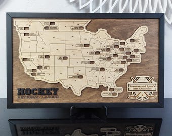 May include: A wooden map of the United States with hockey arena locations, framed in black. The map is laser-cut with state outlines and arena names. The text "HOCKEY NATIONAL LEAGUE" is at the bottom. Includes the text "Brendan and Lynn's NHL Adventures".