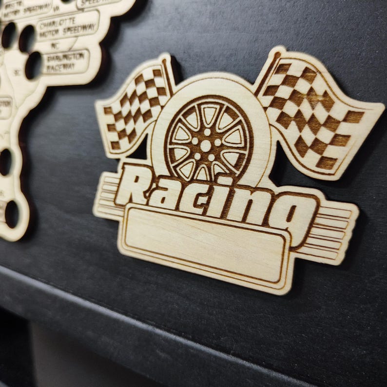 Pu&ograve; includere: Un ritaglio in legno di uno pneumatico da corsa con bandiere a scacchi e la parola "Racing" in un carattere stilizzato. Il ritaglio ha uno spazio vuoto per la personalizzazione.