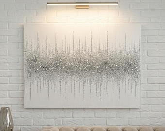 Puede incluir: Una pieza de arte mural rectangular con fondo de lienzo blanco y una banda horizontal central de purpurina plateada y textura de vidrio triturado que se extiende verticalmente en líneas finas y dispersas, iluminada por una lámpara metálica.
