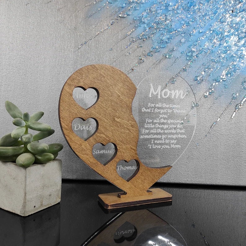 May include: A wooden heart-shaped plaque with a clear acrylic heart insert. The wooden heart has four smaller heart cutouts with the names Dais, Samue, Thoma, and a larger heart cutout with the name "Mom". The acrylic heart insert has a message engraved on it that reads "For all the times that I forgot to thank you, for all the special little things you do, for all the words that sometimes go unspoken I need to say "I love you, Mom".