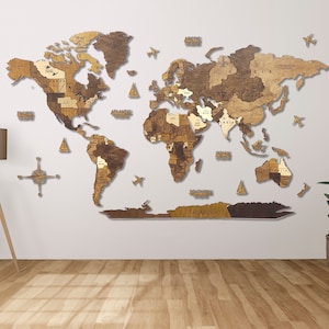 Puede incluir: Un mapa del mundo de madera con un acabado marr&oacute;n claro. El mapa est&aacute; montado en una pared blanca e incluye una br&uacute;jula y peque&ntilde;os aviones. El mapa est&aacute; hecho de piezas individuales de madera que se ensamblan para formar los continentes.