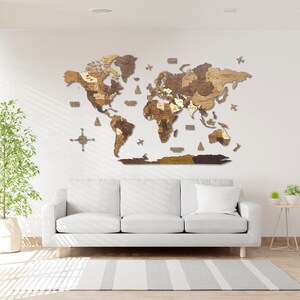 Puede incluir: Un mapa del mundo de madera con un acabado marr&oacute;n claro, montado en una pared blanca sobre un sof&aacute; blanco. El mapa est&aacute; hecho de piezas individuales de madera que se ensamblan para formar los continentes. El mapa est&aacute; rodeado por una pared blanca y un sof&aacute; blanco.