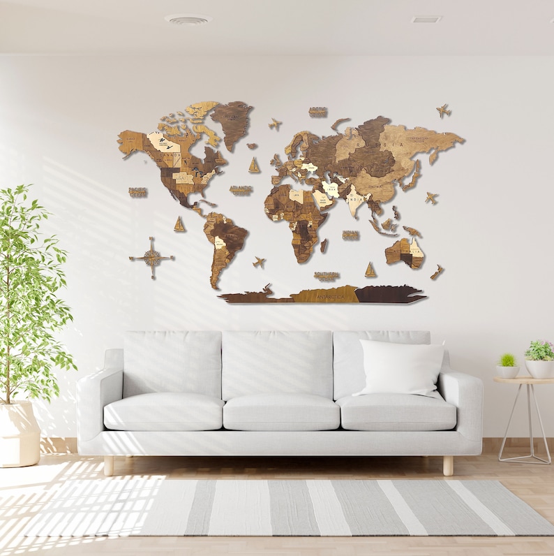 Puede incluir: Un mapa del mundo de madera con un acabado marr&oacute;n claro, montado en una pared blanca sobre un sof&aacute; blanco. El mapa est&aacute; hecho de piezas individuales de madera que se ensamblan para formar los continentes. El mapa est&aacute; rodeado por una pared blanca y un sof&aacute; blanco.