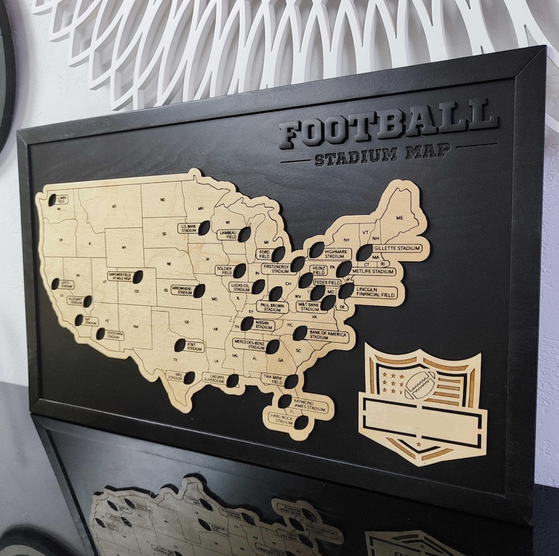 May include: A black framed wooden map of the United States with a brown wood cutout of the country. The map shows the locations of different football stadiums across the country. The title "FOOTBALL STADIUM MAP" is at the top of the map.