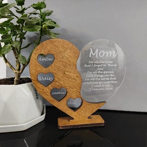 May include: A wooden heart-shaped plaque with a clear acrylic heart attached. The wooden heart has four smaller hearts with the names Amber, Daisy, Samuel, and Thomas inscribed on them. The acrylic heart has the text "Mom" and a message of appreciation for a mother.