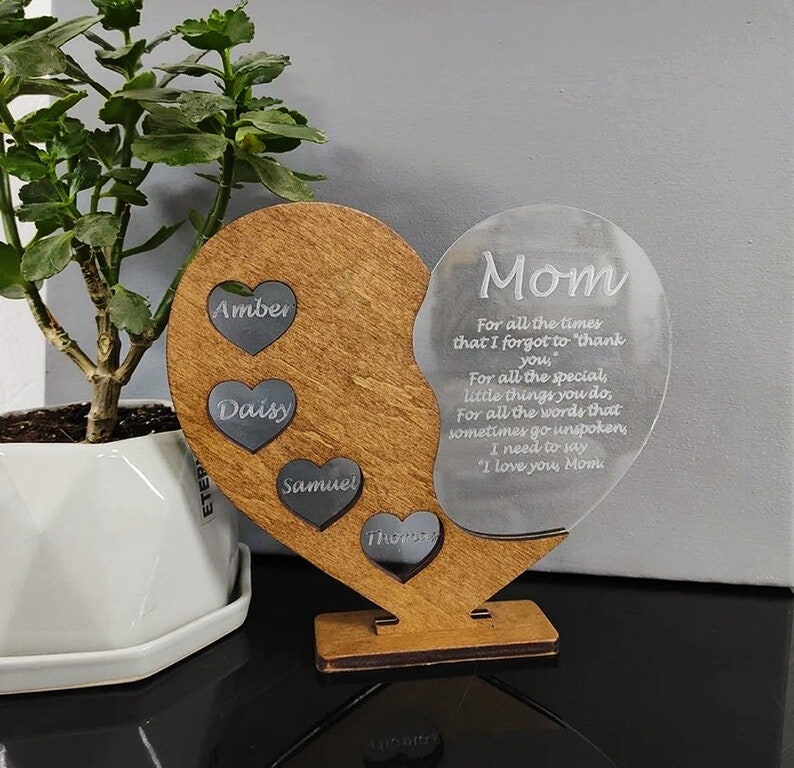 May include: A wooden heart-shaped plaque with a clear acrylic heart attached. The wooden heart has four smaller hearts with the names Amber, Daisy, Samuel, and Thomas inscribed on them. The acrylic heart has the text "Mom" and a message of appreciation for a mother.
