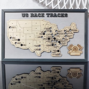 Pu&ograve; includere: Una mappa in legno degli Stati Uniti con punti neri che segnano le posizioni degli autodromi americani. La mappa &egrave; incorniciata da una cornice grigia e ha il testo "US Race Tracks" in alto. L'angolo in basso a destra della mappa ha un cartello in legno che dice "Racing" con una bandiera a scacchi e una gomma.