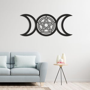 Puede incluir: Decoración de pared de metal negro con un símbolo de triple luna con un pentagrama en el centro. La decoración está montada en una pared blanca sobre un sofá azul claro.
