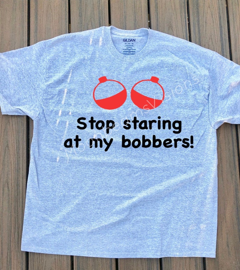May include: A grey t-shirt with a humorous fishing-themed graphic. The graphic features two red fishing bobbers and the text "Stop staring at my bobbers!"