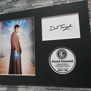 May include: A black framed autograph display featuring a photo of David Tennant as the Doctor from Doctor Who. The display includes a signed autograph and a limited edition number of 002/100.