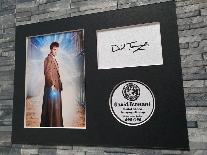 May include: A black framed autograph display featuring a photo of David Tennant as the Doctor from Doctor Who. The display includes a signed autograph and a limited edition number of 002/100.