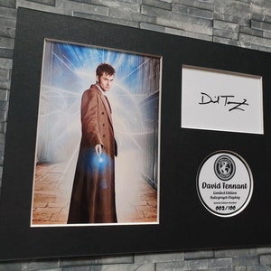 May include: A black framed photograph of David Tennant, the tenth Doctor Who, in a brown coat, standing in a futuristic setting. The photo is signed "David Tennant" and includes a limited edition autograph display numbered 603/100.