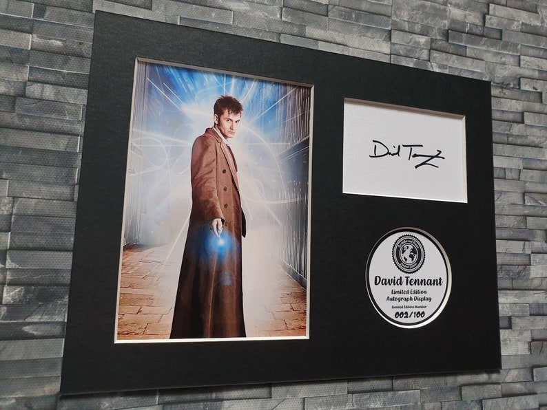 May include: A black framed photograph of David Tennant, the tenth Doctor Who, in a brown coat, standing in a futuristic setting. The photo is signed "David Tennant" and includes a limited edition autograph display numbered 603/100.