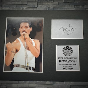 May include: A black framed photo of Freddie Mercury singing into a microphone. The photo is part of a limited edition autographed display, numbered 003/100. The signature is in silver ink.