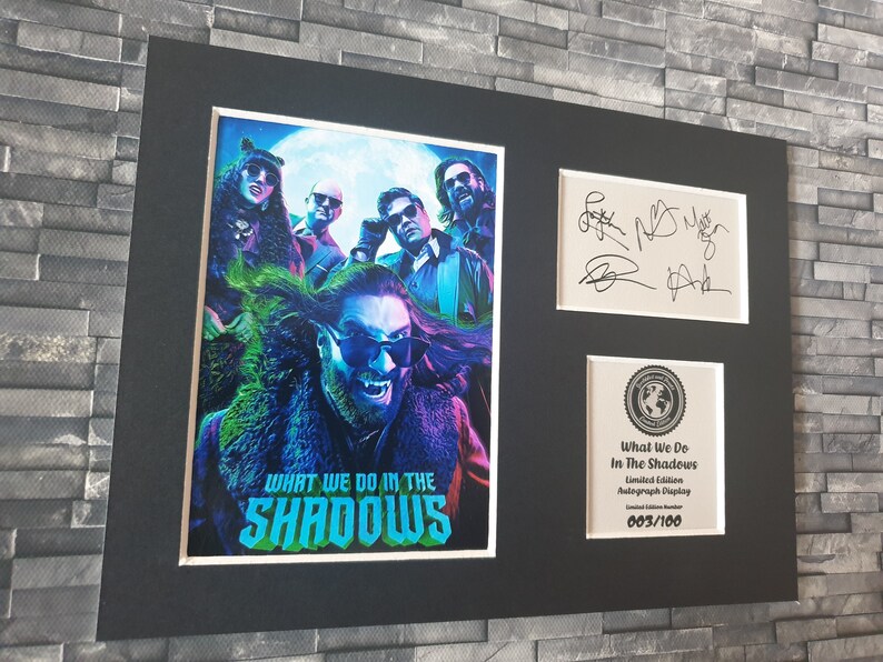 Pu&ograve; includere: Un poster incorniciato del cast della serie TV "What We Do in the Shadows" con le loro autografi. Il poster presenta un'immagine in nero e verde del cast su uno sfondo di luna piena. La cornice &egrave; nera con un bordo argentato. Il poster &egrave; numerato 003/100.