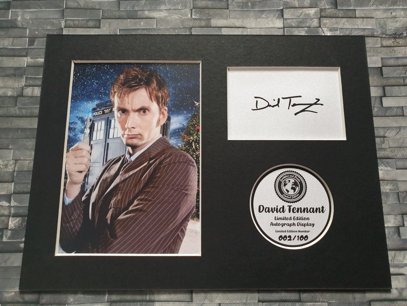 May include: A black framed photograph of David Tennant, the tenth Doctor Who, holding a sonic screwdriver. The photo is signed "David Tennant" and includes a limited edition autograph display with the number 002/100.