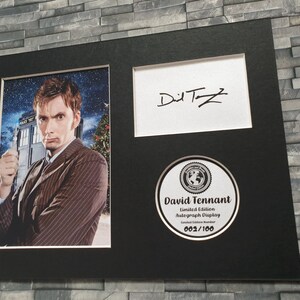 May include: A black framed photograph of David Tennant, the tenth Doctor Who, in a brown striped suit, holding a sonic screwdriver. The photograph is signed "David Tennant" in black ink. The photograph is part of a limited edition autograph display, numbered 002/100.