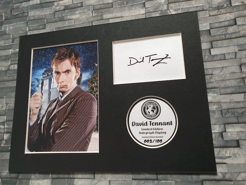 May include: A black framed photograph of David Tennant, the tenth Doctor Who, in a brown striped suit, holding a sonic screwdriver. The photograph is signed "David Tennant" in black ink. The photograph is part of a limited edition autograph display, numbered 002/100.