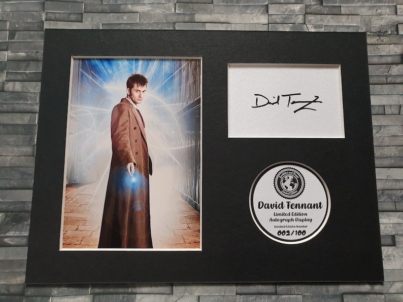 May include: A black framed photograph of David Tennant, the tenth Doctor Who, wearing a brown coat. The photo is signed "David Tennant" and includes a limited edition autograph display numbered 002/100.
