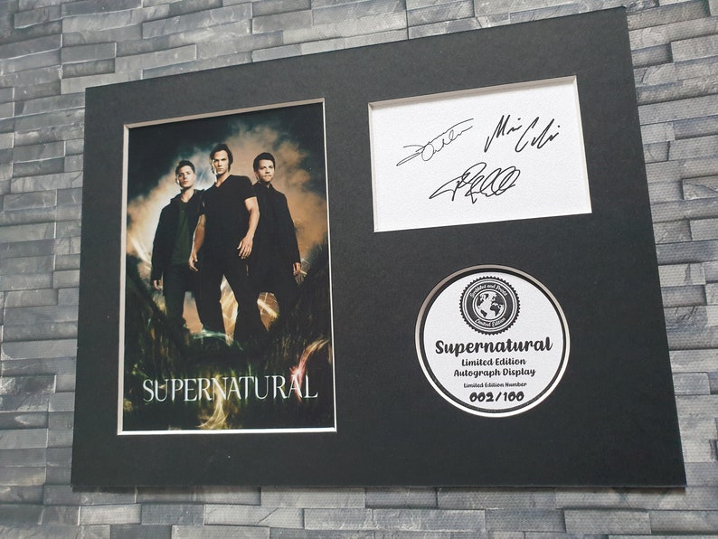 May include: A black framed print of a photo of three men from the TV show Supernatural. The print has a black and white signature, a Supernatural logo, and the text "Limited Edition Autograph Display 002/100".