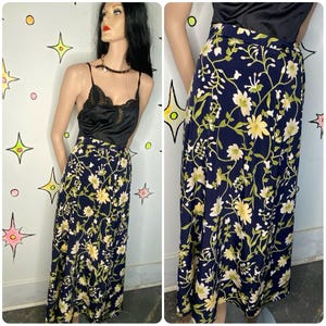 May include: A long, navy blue skirt with a floral pattern featuring yellow and white flowers and green vines. The skirt is paired with a black lace camisole. The skirt is displayed on a mannequin.