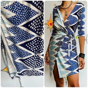 May include: A wrap dress with a geometric pattern in shades of blue and white. The dress features a V-neckline, long sleeves, and a tie waist. The fabric has a design of triangles and dots.