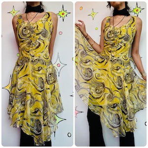 May include: A sleeveless yellow dress with a swirling pattern in shades of gray and brown. The dress has a unique asymmetrical hemline and a gathered bodice. The model is wearing black pants. The background is a white wall with star and circle designs.