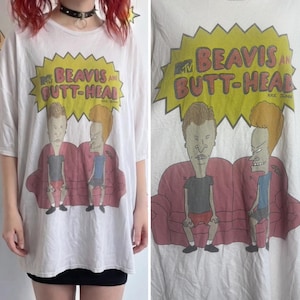 May include: White t-shirt featuring the animated characters Beavis and Butt-Head sitting on a red couch. The shirt has the MTV logo and the text "BEAVIS AND BUTT-HEAD" in a yellow burst. The design is a vintage style.