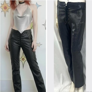 May include: Black leather pants with a high waist and decorative stitching. The pants have a lace-up detail at the front and a fitted silhouette. The image also shows a silver halter top.
