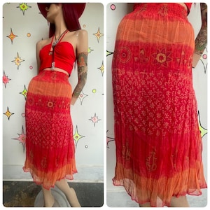 May include: A mid-length skirt featuring a vibrant gradient of red and orange hues. The fabric displays a tiered design with a smocked elastic waistband and intricate patterns including floral motifs, small dots, and paisley-like shapes.