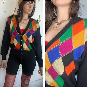 May include: Black cardigan sweater with a colorful argyle pattern in gold, orange, green, blue, and pink. The sweater has a V-neck, long sleeves, and gold buttons. The argyle pattern is on the front and shoulders.
