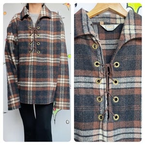 May include: A brown, black, and cream plaid shirt with a lace-up front. The shirt has a collared neckline and long sleeves. The lace-up detail features gold-colored grommets and brown cording. The shirt is a vintage style.