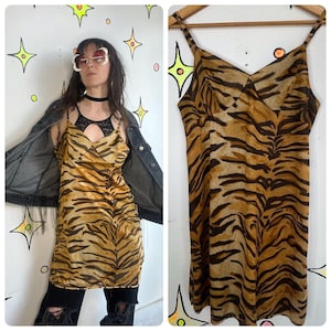 Op de afbeelding: Een slipdress in vintage-stijl met een tijgerstreepmotief in bruin- en beigetinten. De jurk heeft dunne spaghettibandjes en een V-hals. De jurk wordt getoond op een houten hanger en ook gedragen door een persoon.