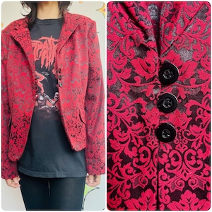 May include: A red blazer with a black floral pattern and three black buttons. The blazer is worn over a black graphic t-shirt. The blazer has a notched lapel and two front pockets.