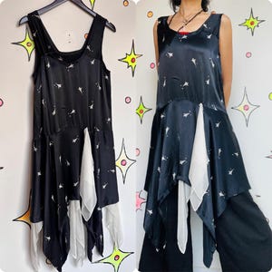 May include: A black satin dress with a white chiffon overlay. The dress has a fitted bodice and a flowing skirt with a high-low hemline. The dress is decorated with a small, white star pattern.
