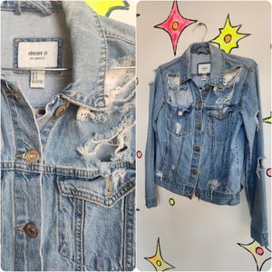 May include: Light blue denim jacket with distressed details and a Forever 21 Los Angeles label. The jacket has several rips and tears throughout, giving it a vintage look.