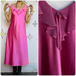 May include: A bright pink maxi dress with a ruffled neckline and a tie detail. The dress has a flowing silhouette and is made of a shiny fabric. The dress is sleeveless and has a V-neckline.