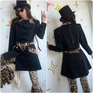 May include: Black blazer with leopard print accents, paired with matching leopard print pants. The blazer features a gold chain belt and a top hat. The outfit is styled with sunglasses.