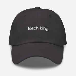 Puede incluir: Gorra de béisbol gris oscuro con el texto bordado "fetch king" en blanco. La gorra tiene una visera curva y una corona estructurada, adecuada para uso casual.